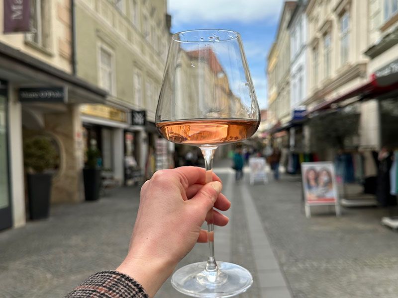 A handle holding up a glass of wine in front of a street. 