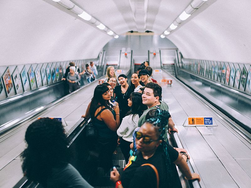 A group of people smiling and laughing on a London Underground escalator