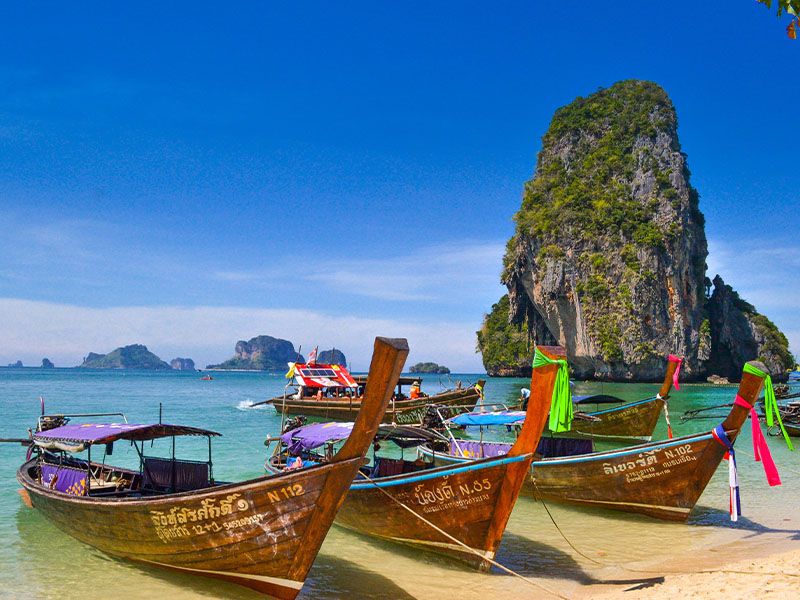 Traditional Thai boats moored on a beach with islands and the ocean in the background.