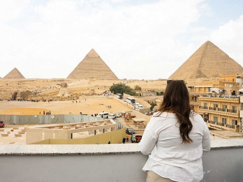 Woman standing on a balcony overlooking the Great Pyramids. 