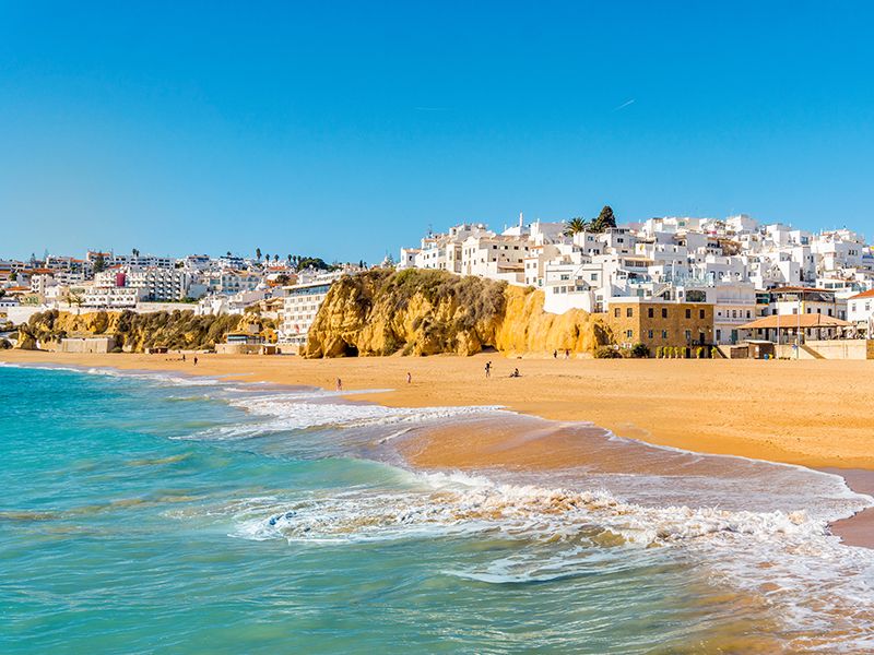 Beach with crashing waves and white-washed buildings in background in Algarve