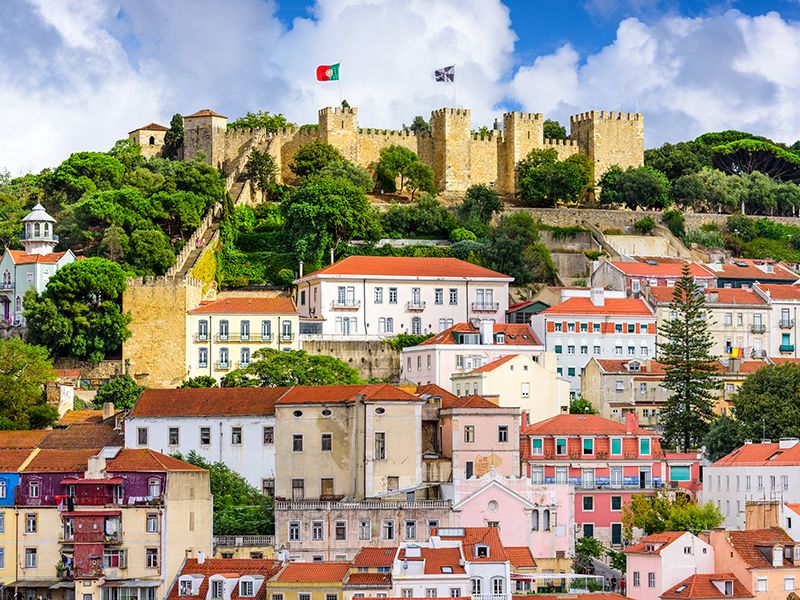 Sao Jorge Castle on top of a hill with flags waving and orange roofed buildings in foreground