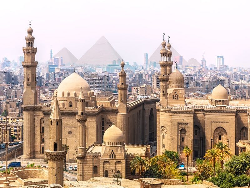 A mosque and the Cairo city skyline with the three pyramids in the distance