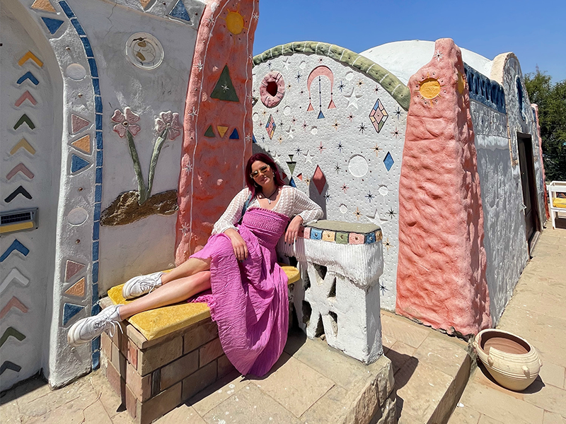 A woman reclining on a bench in front of a colorful building.