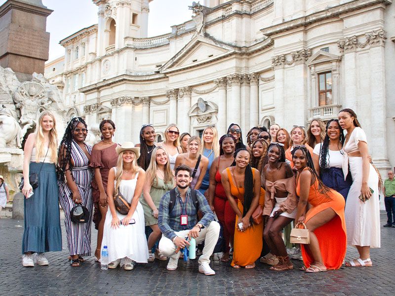 A group of people posing and smiling in front of a grand stone building. 