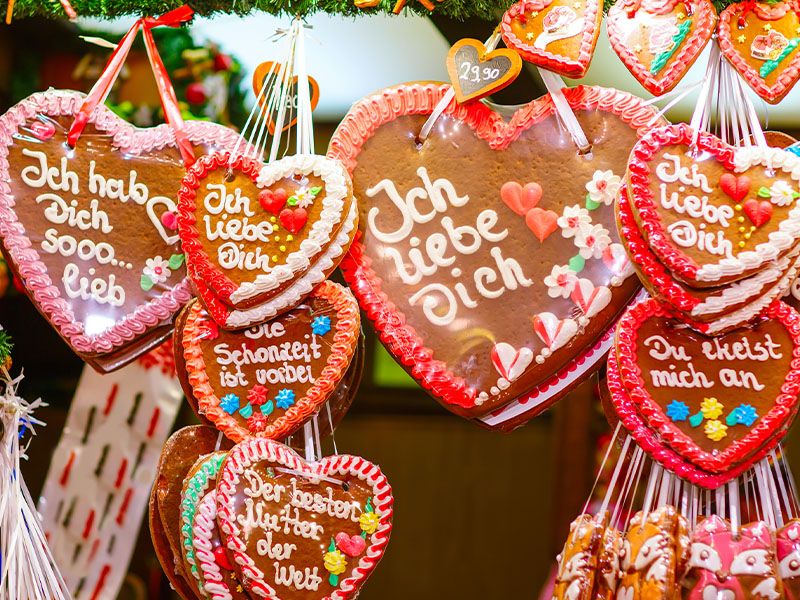 Several gingerbread cookies shaped like hearts with german phrases written on them with frosting