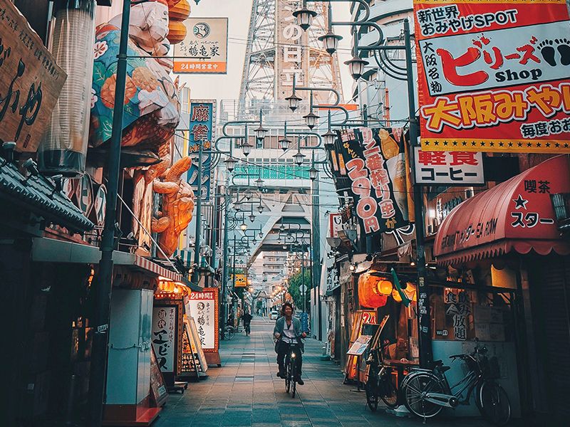 A man riding a bike through a narrow street in Shinsekai, Osaka.