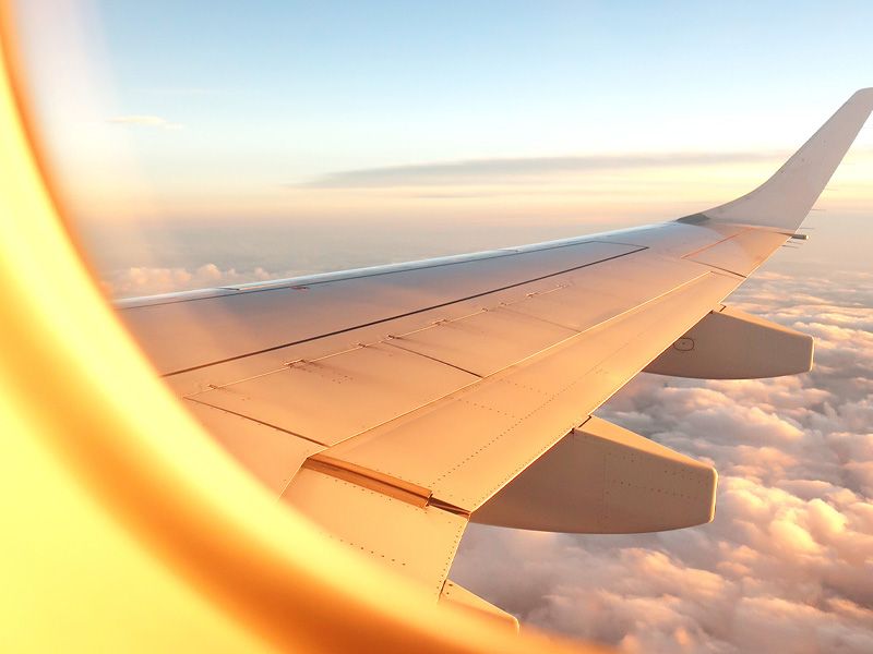 an image of a window from the inside of a plane looking out at the plane wing over the clouds