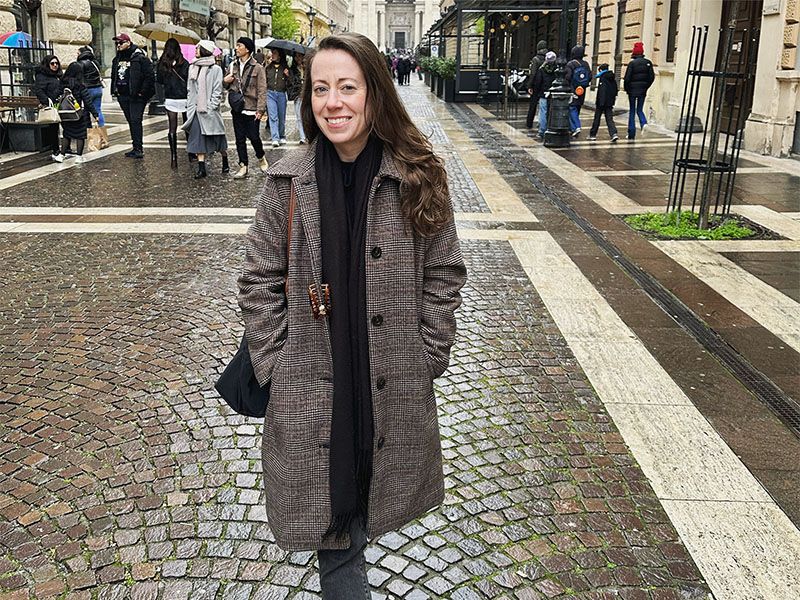 A woman smiling in front of a busy stone street.