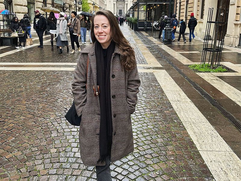 A woman smiling in front of a busy stone street. 