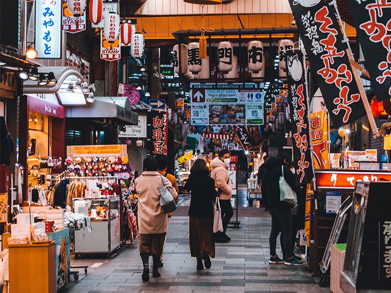 People walking through the shopping stalls of Kuromon Market.