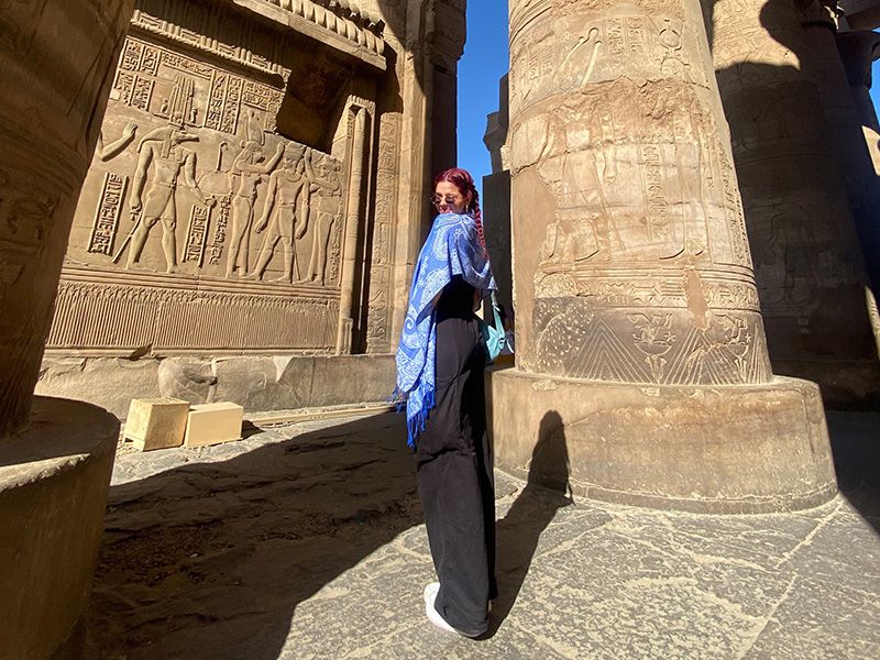 Woman looking over her shoulder in front of a carved stone column and wall. 