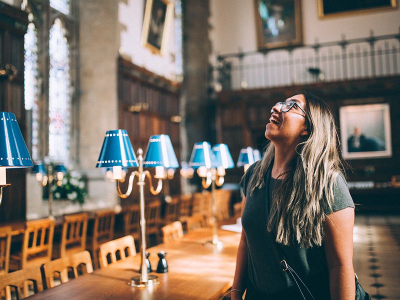 A woman smiling and looking up in awe in Christ Church dining hall at Oxford University