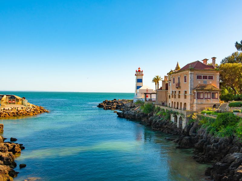 Blue ocean with quaint house and lighthouse along the shore in Sintra