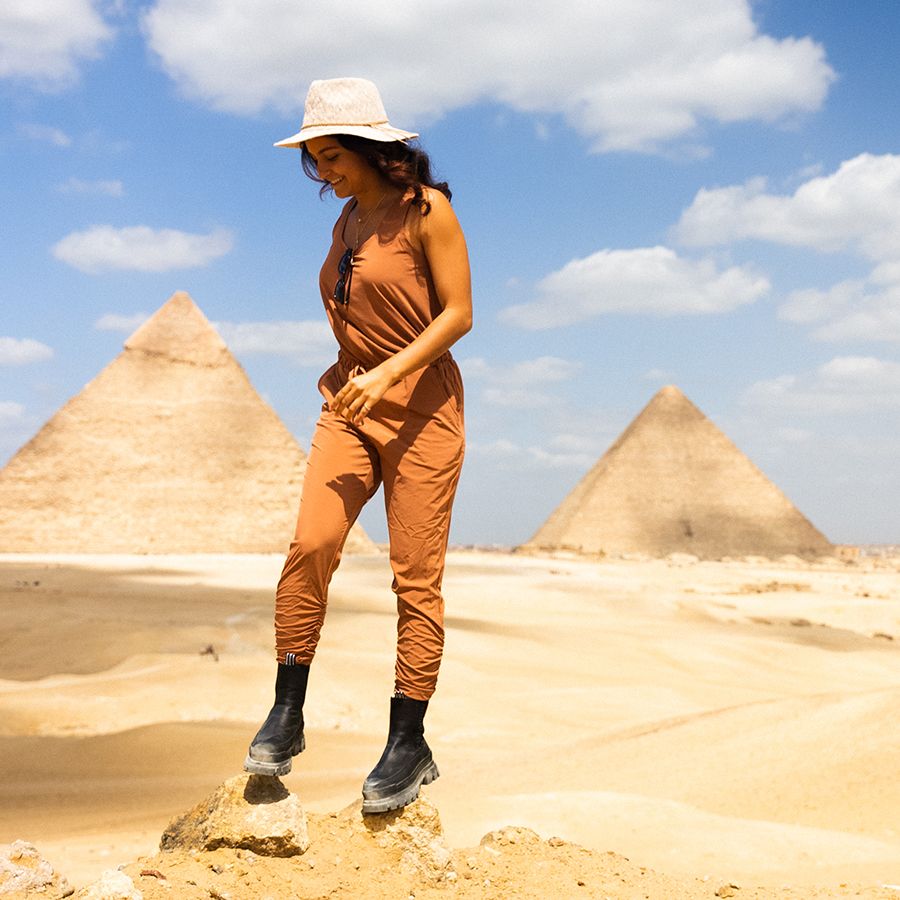 A woman smiling and walking with the Great Pyramids in the background.