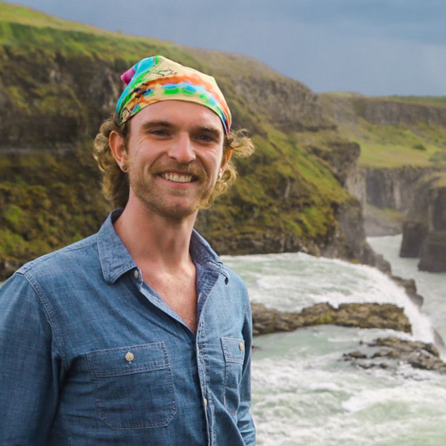 A man smiling for a photo and standing in front of a large waterfall