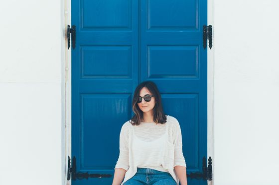 a woman sitting in front of a bright blue door on a traditional greek whitewashed building