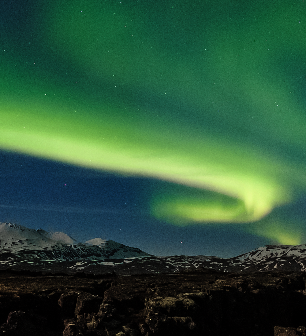 green northern lights floating above mountains in iceland