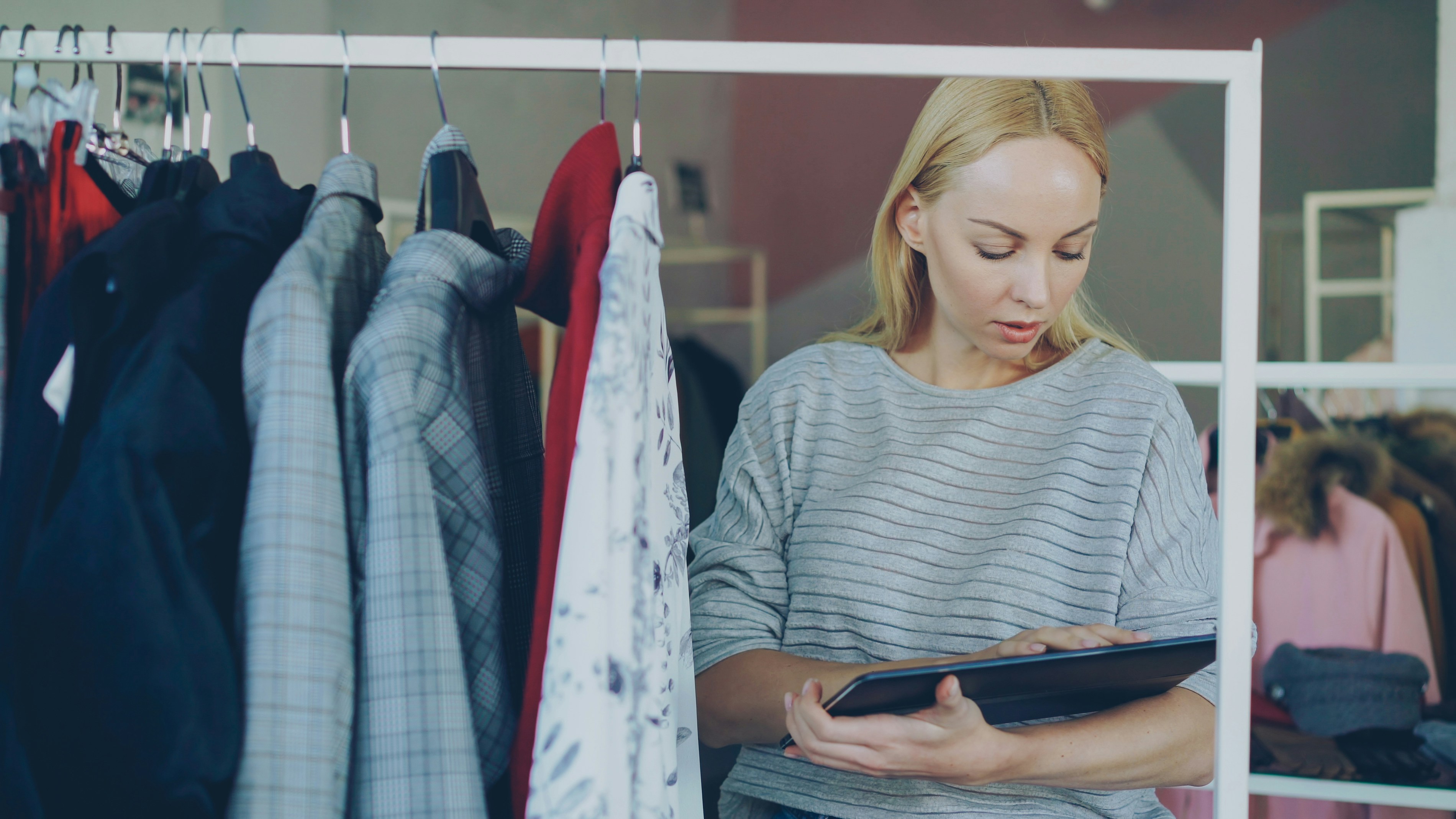 Retail manager using a tablet while checking inventory on clothing rails