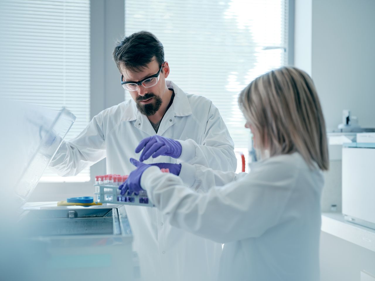 Un homme travaille dans un Laboratoire avec une collègue. Ils récupèrent des tubes à essai.