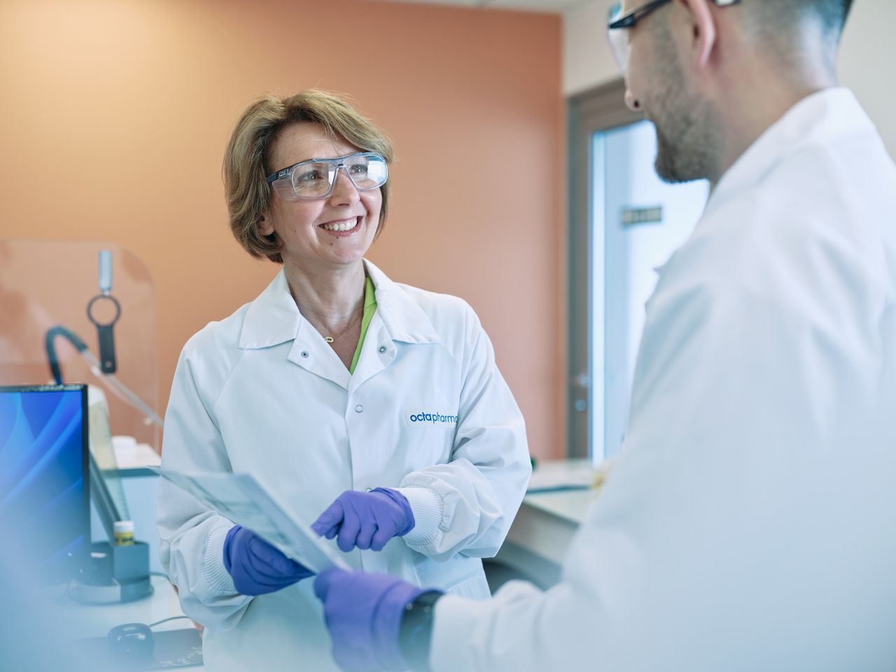 Une femme, dans un laboratoire, discute avec un collègue. Elle lui montre une ligne sur un document.