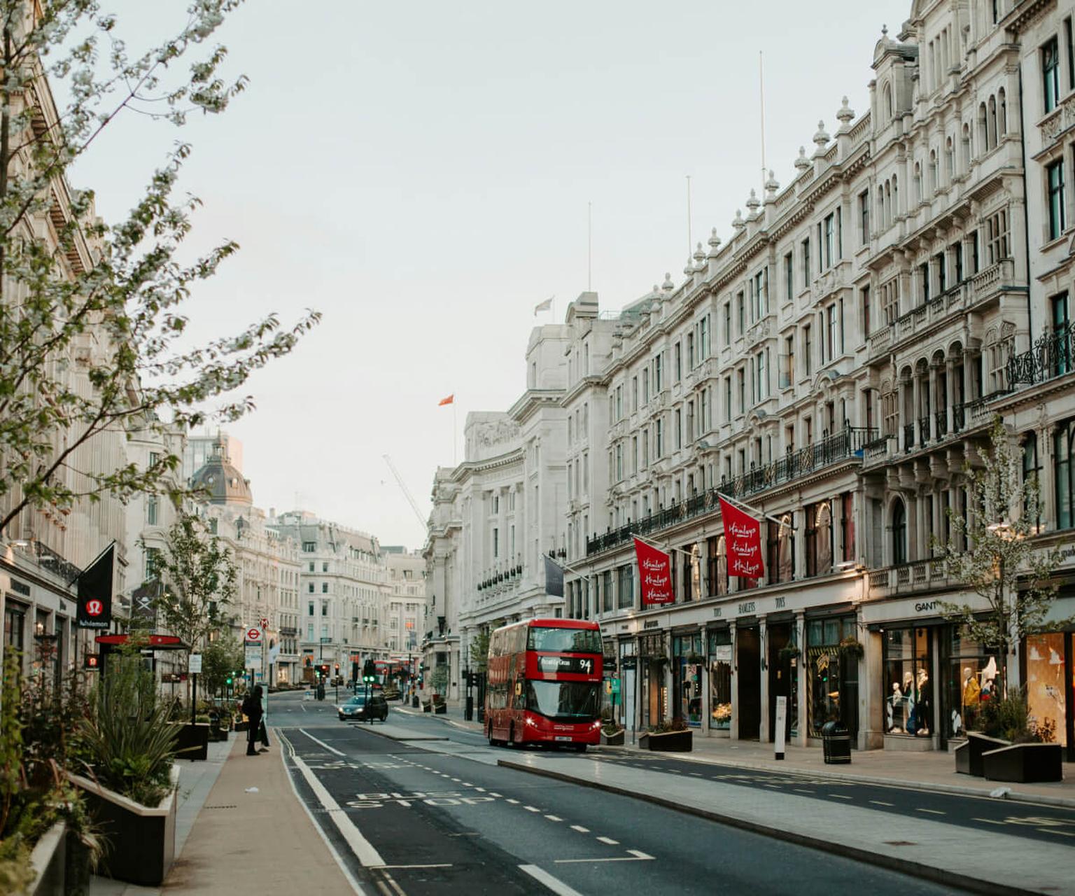 Typical London street with red double-decker buses, historic buildings, and shops.