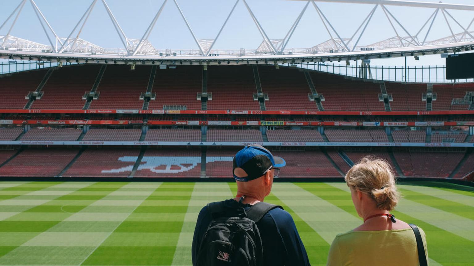 Two visitors in the stands of a football stadium in London overlooking the pitch.