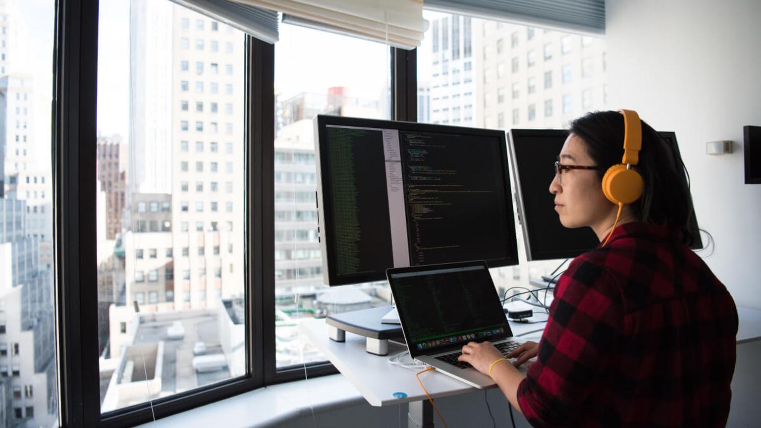 Young man wearing headphones working at a computer in a bright office.
