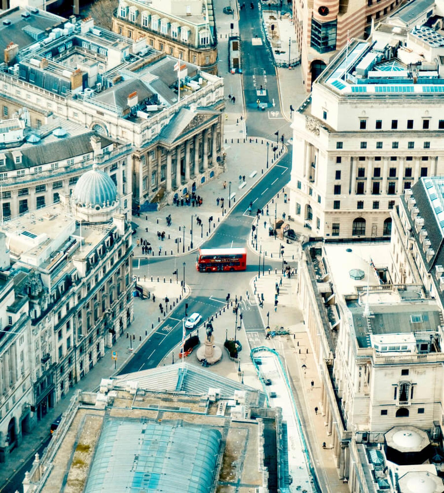 Aerial view of a busy street in central London with city buildings and red double-decker buses.