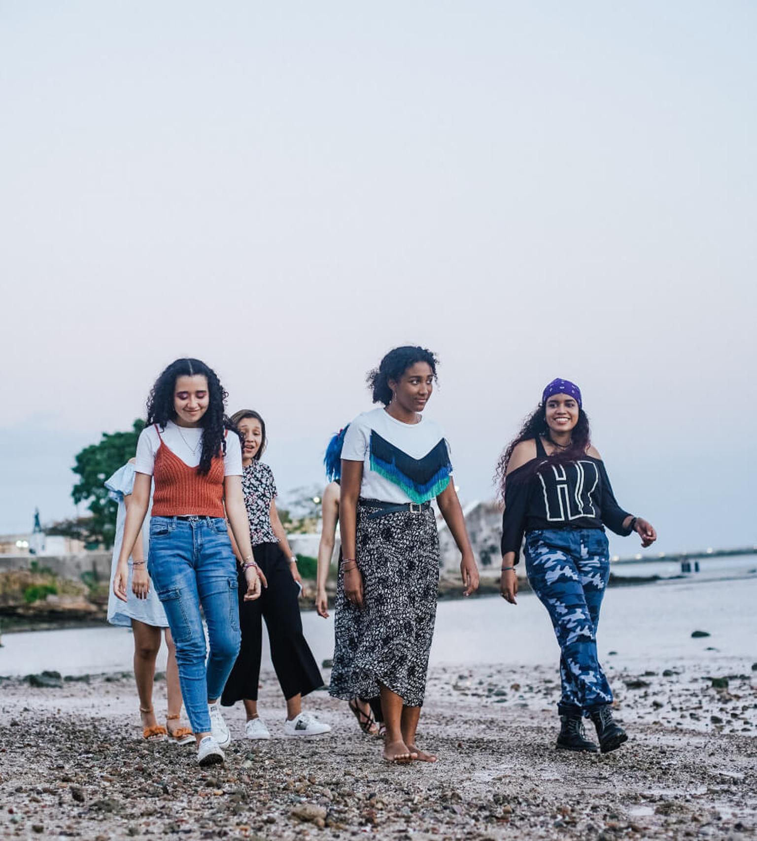 A group of young women walking together along a pebble beach.