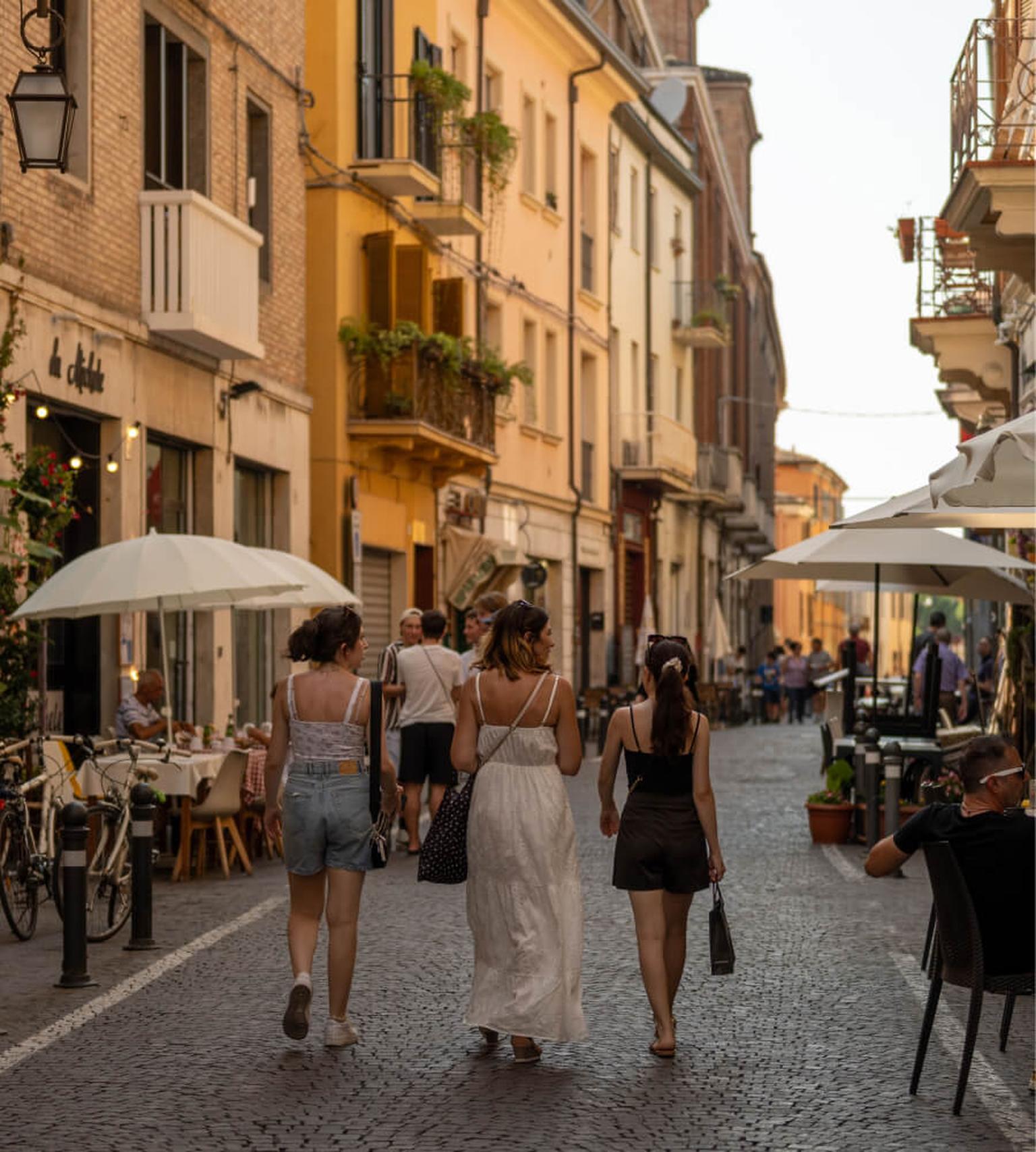 Junge Menschen spazieren durch eine italienische Altstadt mit Cafés und Restaurants