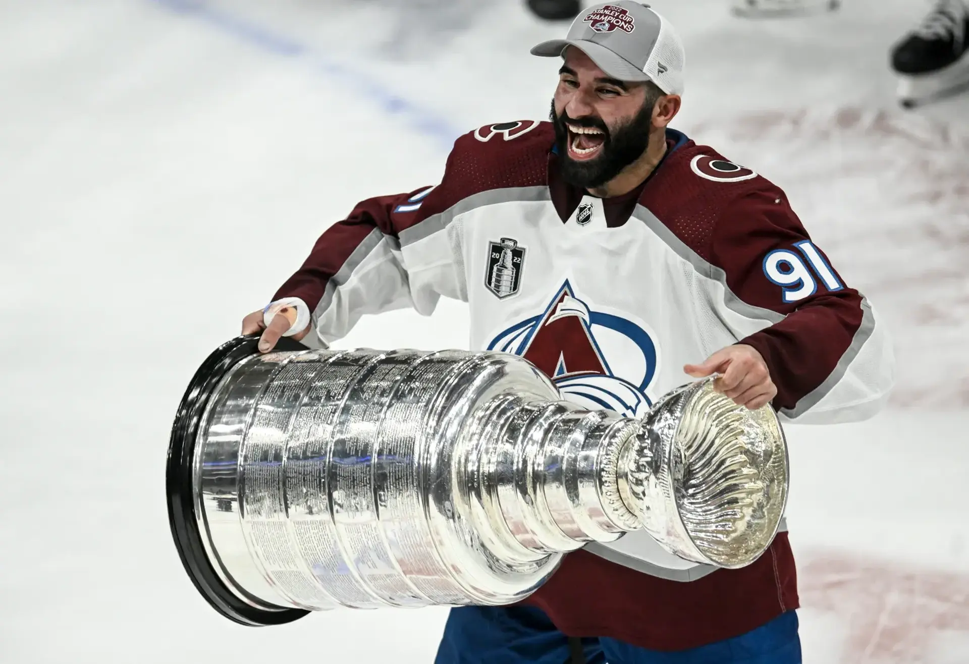 Nazem Kadri smiling while hoisting the stanley cup in front of him.