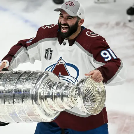 Nazem Kadri smiling while hoisting the stanley cup in front of him.