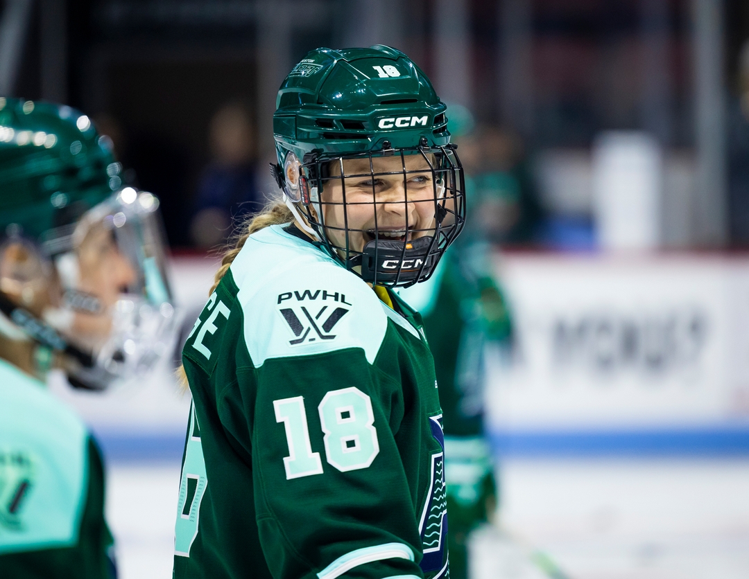 Jessie Eldridge in green Boston Fleet jersey, numbered 18, smiles on the ice during the anthem.