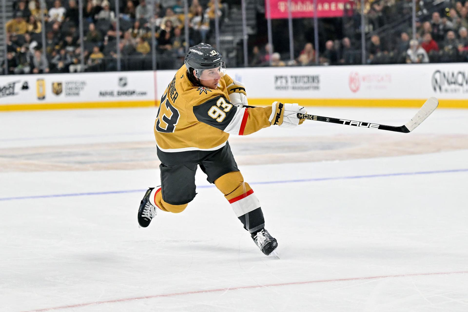 Mitch Marner in a gold Vegas Golden Knights jersey firing a slapshot from inside the blue line.