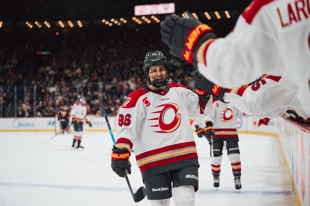 Michela Cava in a white Charge jersey celebrating with teammates near the bench during a game.