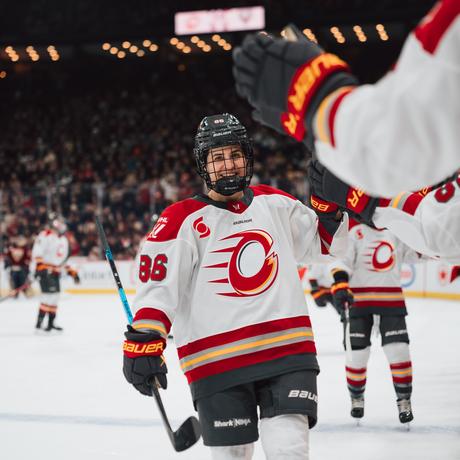 Michela Cava in a white Charge jersey celebrating with teammates near the bench during a game.