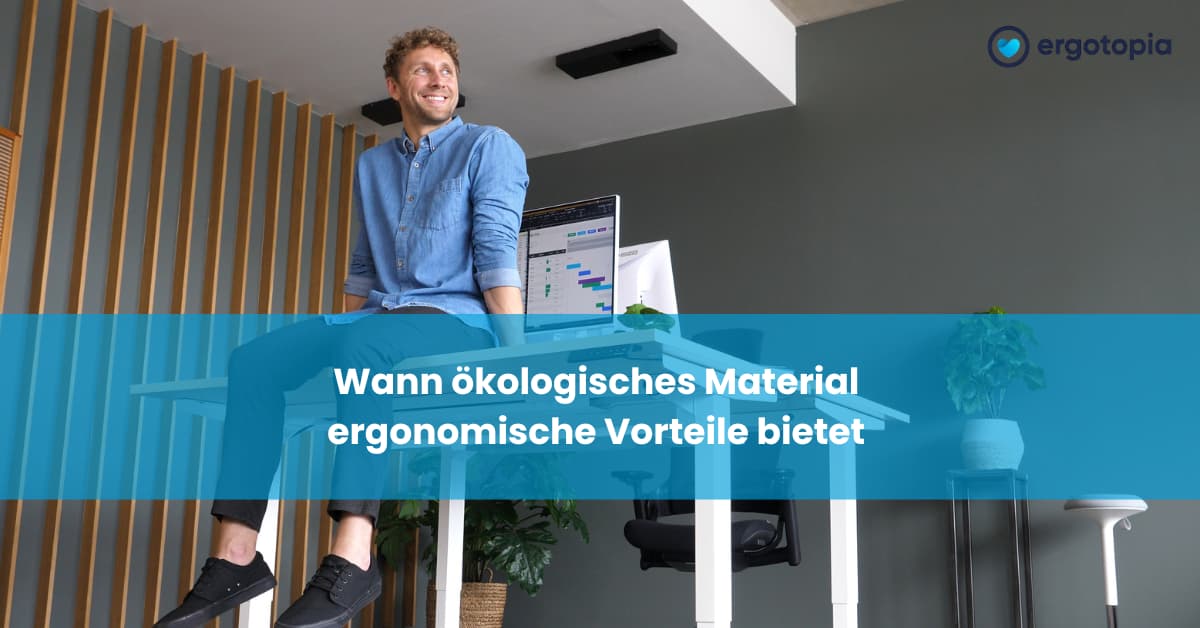 Mann sitzt lächelnd auf Schreibtisch mit Laptop in modernem Holz-Büro mit Pflanzendekoration