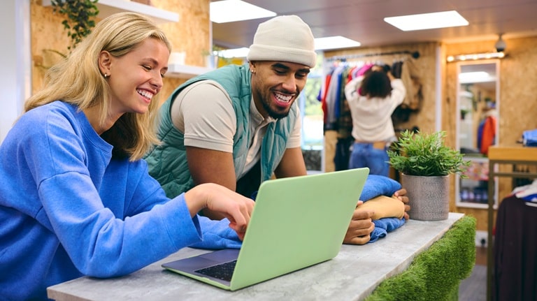 Male and female business owners working at cash desk with laptop in pop-up clothes store Male and female business owners working at cash desk with laptop in pop-up clothes store