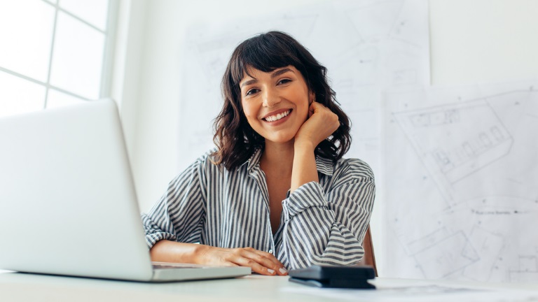 A smiling female architect sitting at her office desk