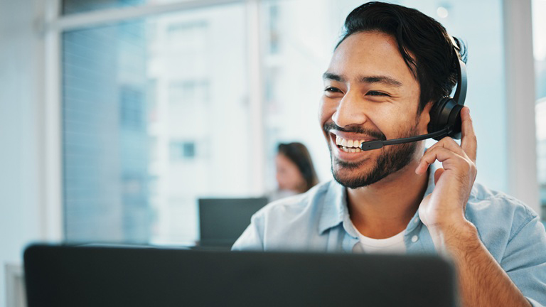 Young Asian IT consultant wearing headset smiling as he provides customer service over the phone
