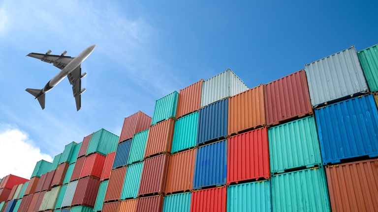 An aeroplane flying over stacks of different coloured shipping containers