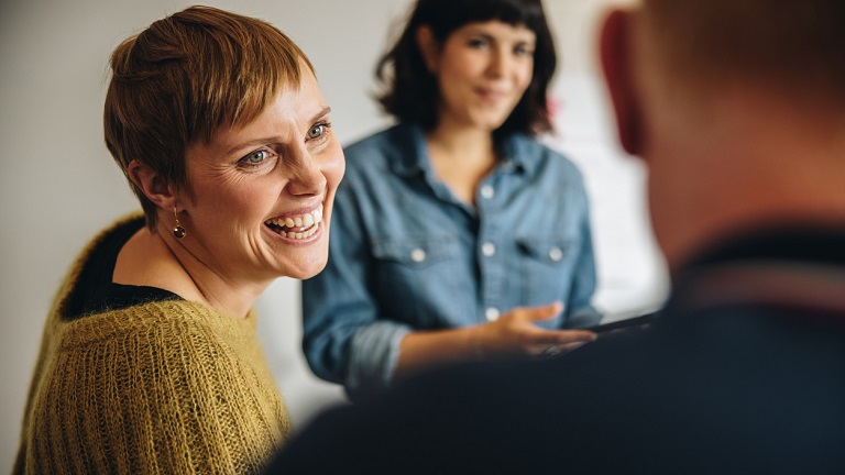 Short-haired woman in group discussion smiling at her unseen colleague