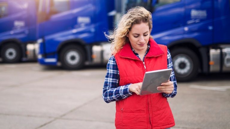 Female truck driver holding tablet and checking route for new destination. In background parked trucks