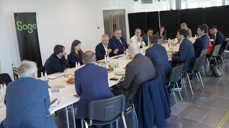 A group of business professionals are engaged in discussion around a large, rectangular conference table in a modern meeting room. The atmosphere is serious and focused.