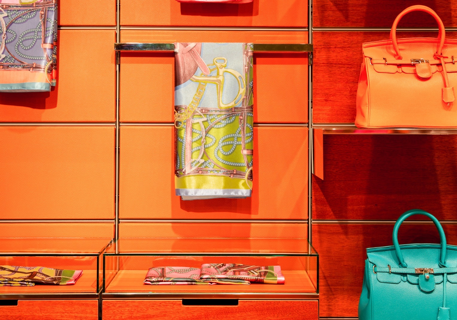 Bright orange panels decorate a wall holding golden shelves displaying various high end fabrics and purses.