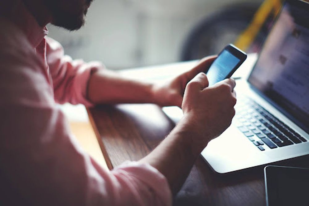 Person using a smartphone and laptop at a desk, illustrating digital outreach strategies for building referral networks and promoting referral programs.