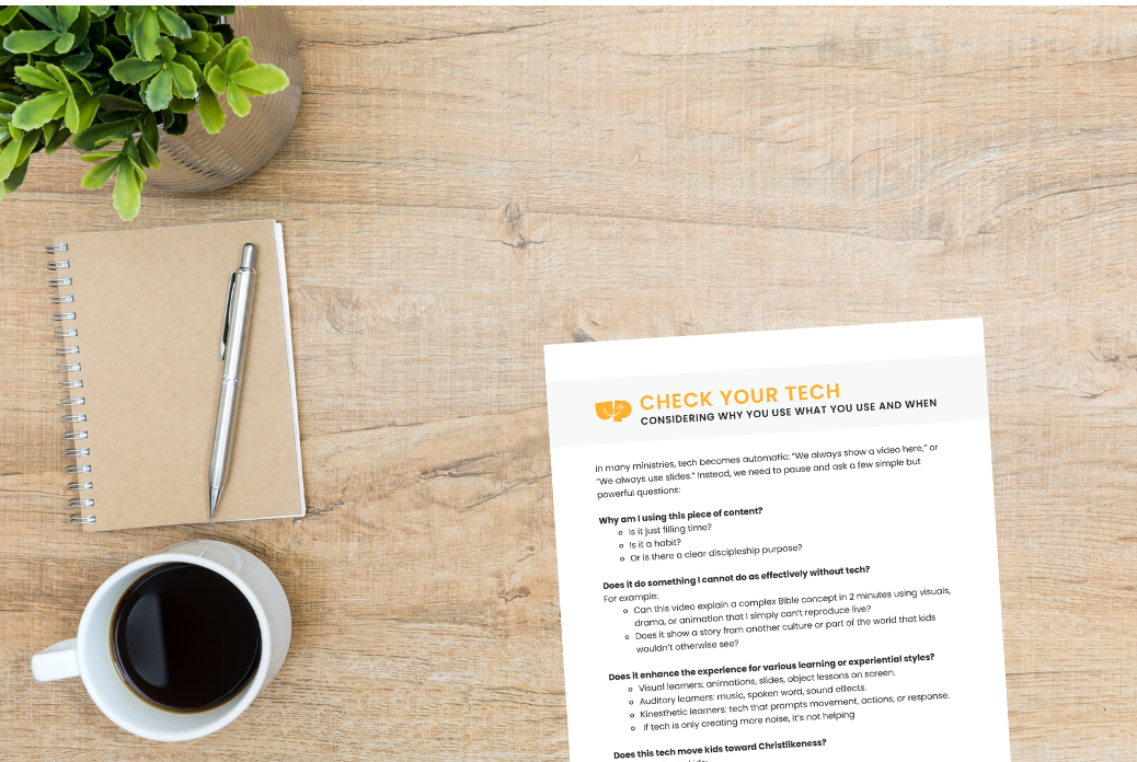 Overhead view of a desk with a notebook, pen, coffee cup, plant, and a printed document titled "CHECK YOUR TECH" with text on technology use.