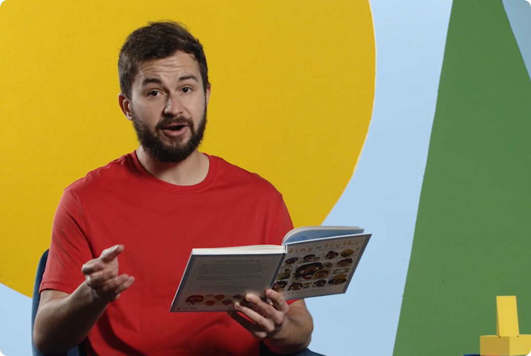 A man in a red shirt holds and reads a children's bible, set against a bright geometric background.