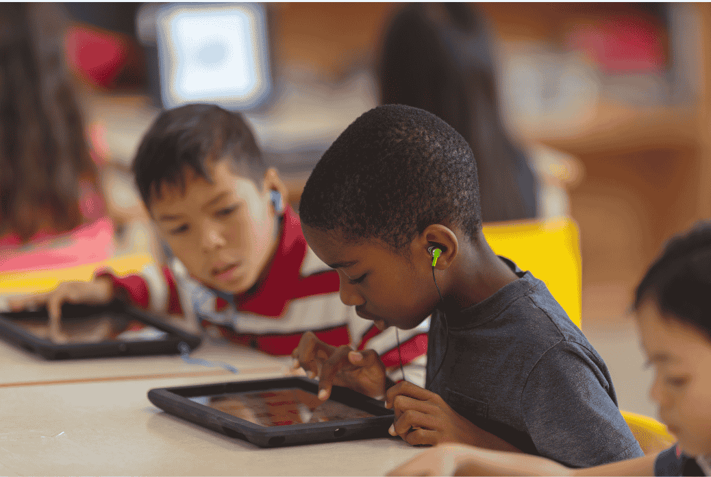 Children using tablets with headphones in a classroom, focused on their screens, engaged in learning activities.